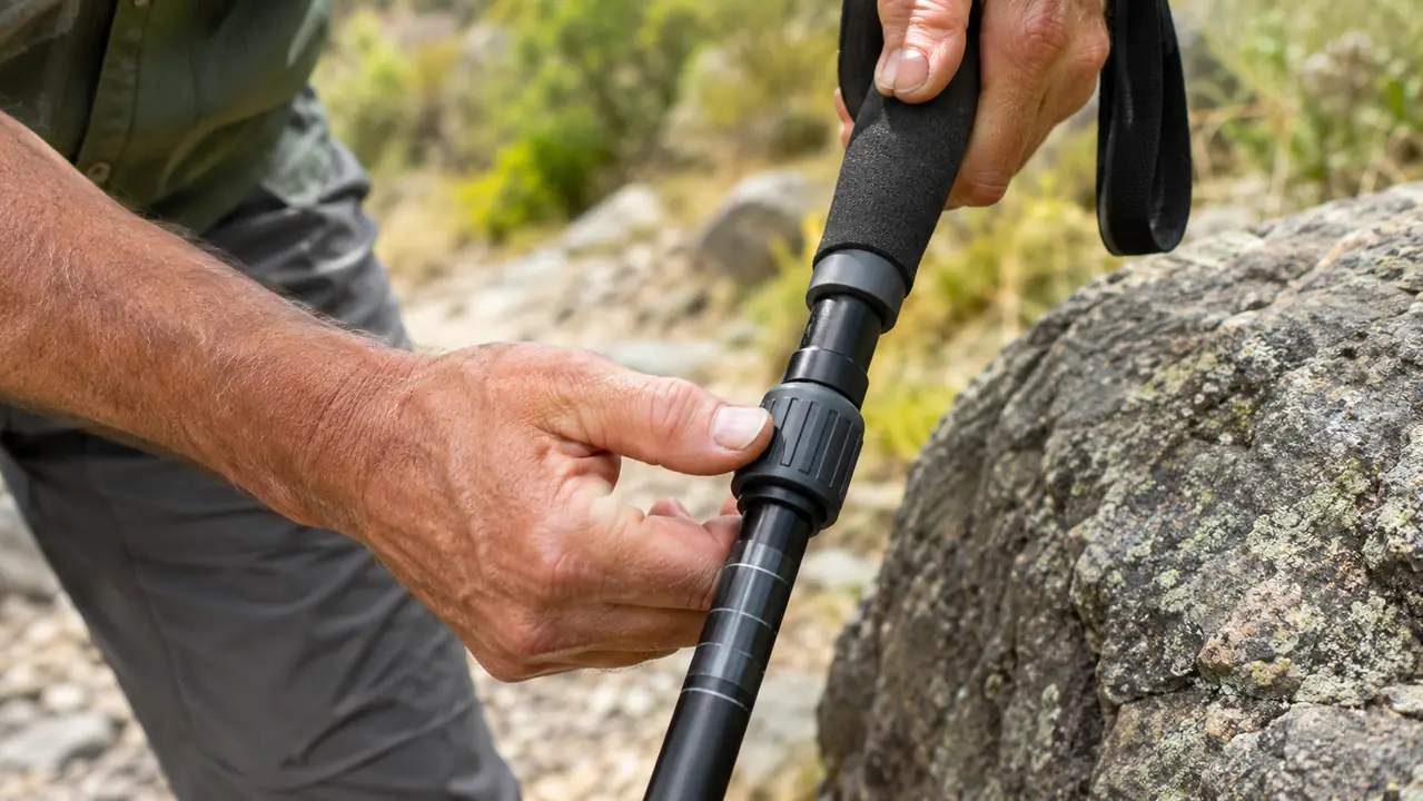 A hand adjusting the length of a trekking pole while the pole rests against a rock